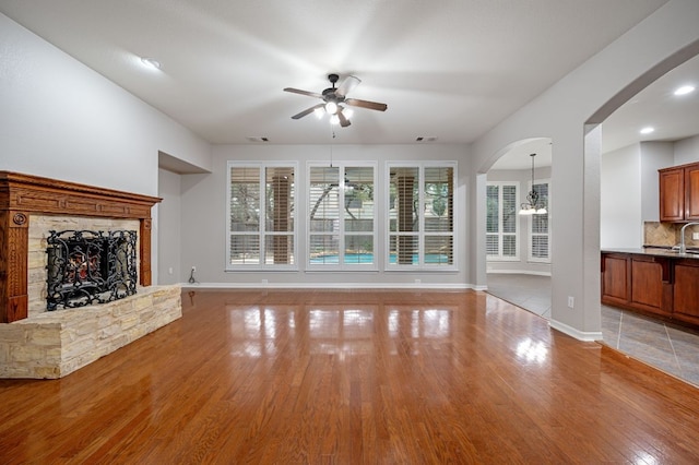 1116 Castle Path, Round Rock, TX 78681 - unfurnished living room with a ceiling fan, light wood-style flooring, a stone fireplace, arched walkways, and a chandelier