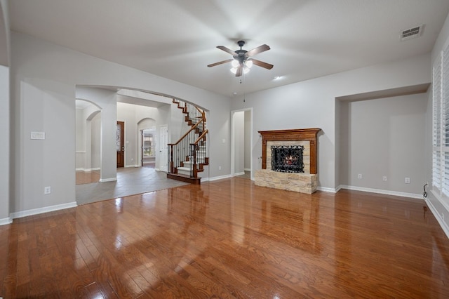 1116 Castle Path, Round Rock, TX 78681 - unfurnished living room featuring arched walkways, ceiling fan, a warm lit fireplace, wood finished floors, and stairs