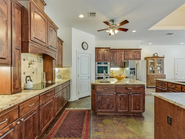 167 Manawianui Dr, Bastrop, TX 78602 - kitchen with stainless steel appliances, ceiling fan, backsplash, light stone countertops, and a kitchen island with sink