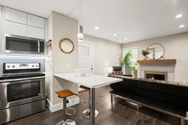935 La Posada Dr Unit 148, Austin, TX 78752 - kitchen with stainless steel appliances, dark wood finished floors, white cabinetry, a kitchen bar, and backsplash