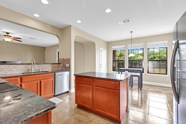 301 Wye Oak St, Austin, TX 78748 - kitchen featuring stainless steel appliances, brown cabinetry, tasteful backsplash, dark stone countertops, and ceiling fan