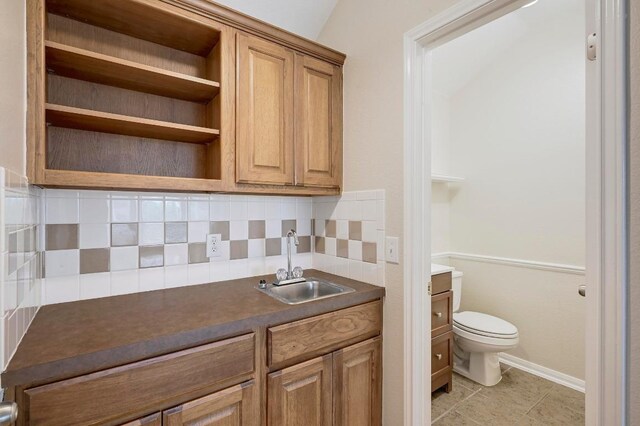 19709 Vilamoura St, Pflugerville, TX 78660 - kitchen featuring dark countertops, backsplash, open shelves, light tile patterned floors, and brown cabinetry