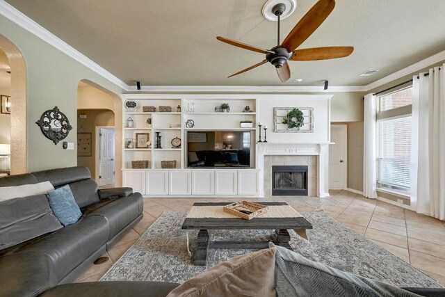 19709 Vilamoura St, Pflugerville, TX 78660 - living room with arched walkways, light tile patterned floors, ceiling fan, crown molding, and a tile fireplace
