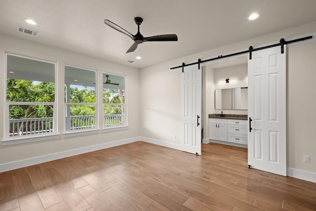 147 Kahana Ln, Bastrop, TX 78602 - unfurnished bedroom featuring a barn door, multiple windows, light wood-style flooring, ensuite bath, and recessed lighting