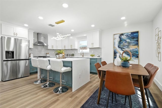 2400 Burly Oak Dr, Austin, TX 78745 - kitchen featuring stainless steel fridge with ice dispenser, wall chimney range hood, light wood-style floors, a center island, and white cabinets