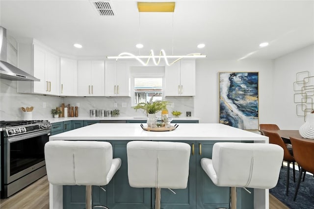 2400 Burly Oak Dr, Austin, TX 78745 - kitchen featuring stainless steel gas range oven, wall chimney exhaust hood, a breakfast bar area, light countertops, and backsplash