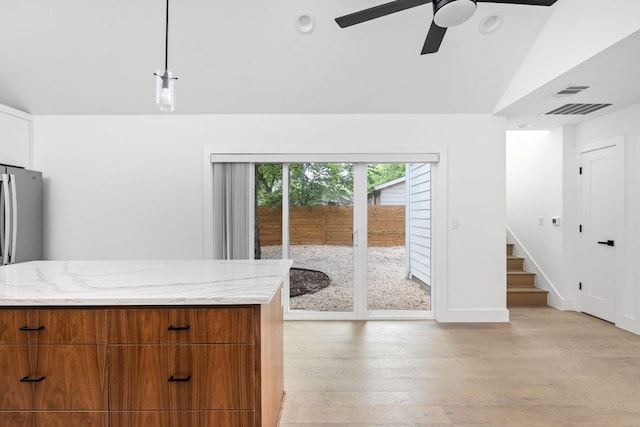 2813 Prado Unit 2, Austin, TX 78702 - kitchen with light stone countertops, a ceiling fan, vaulted ceiling, brown cabinets, and light wood-style floors