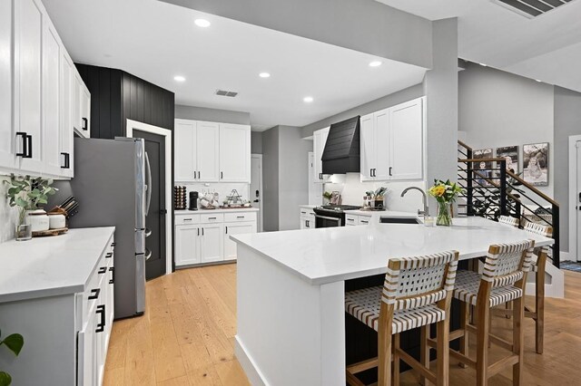 3703 Runnels Ct, Austin, TX 78732 - kitchen with custom range hood, a peninsula, recessed lighting, light wood-style flooring, and a kitchen breakfast bar