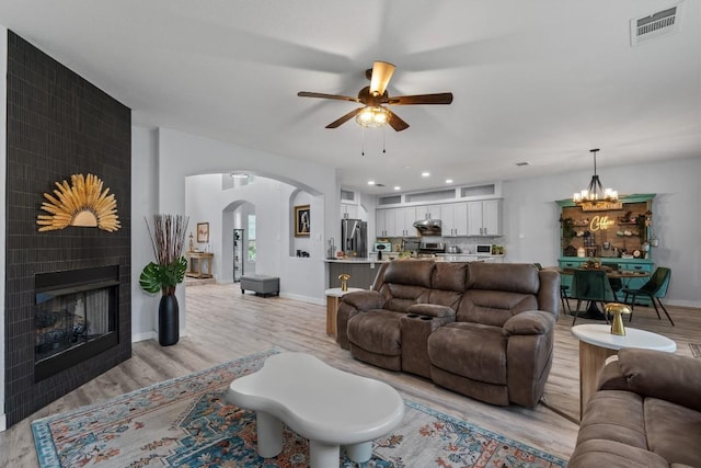 2108 Ariella Dr, Cedar Park, TX 78613 - living area featuring light wood-style floors, ceiling fan, arched walkways, a fireplace, and a chandelier