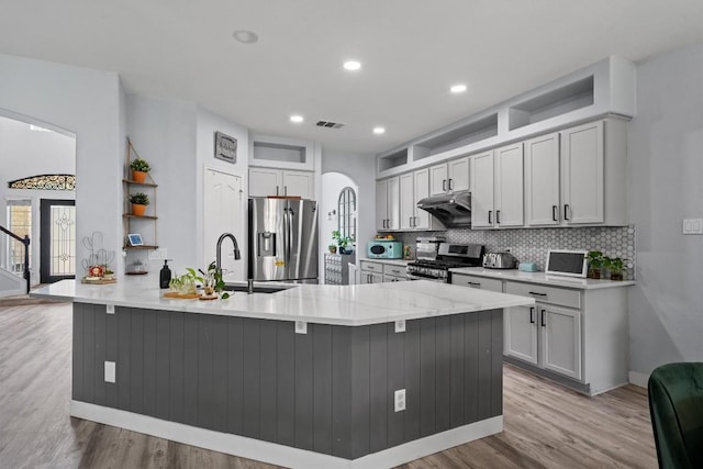 2108 Ariella Dr, Cedar Park, TX 78613 - kitchen with appliances with stainless steel finishes, under cabinet range hood, light wood finished floors, decorative backsplash, and arched walkways