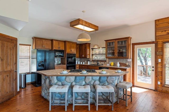 8152 Breeze Way, Jonestown, TX 78645 - kitchen with black appliances, brown cabinetry, backsplash, wood-type flooring, and a breakfast bar area