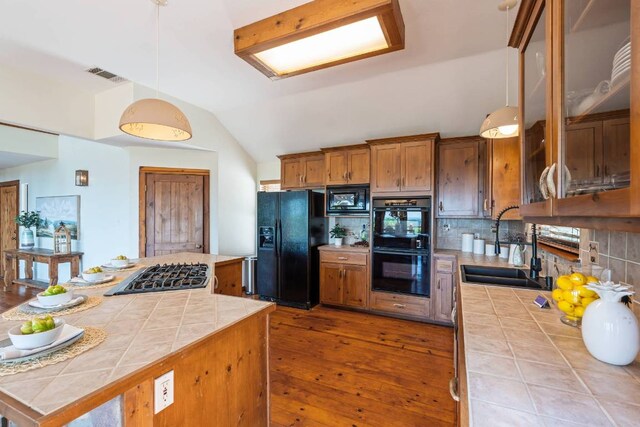 8152 Breeze Way, Jonestown, TX 78645 - kitchen featuring black appliances, tile countertops, brown cabinets, vaulted ceiling, and hardwood / wood-style floors