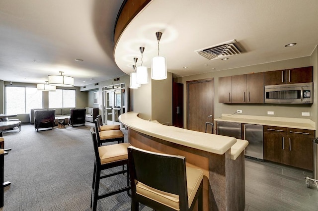 54 Rainey St Unit 1018, Austin, TX 78701 - kitchen featuring stainless steel microwave, dark brown cabinetry, a breakfast bar area, light countertops, and fridge