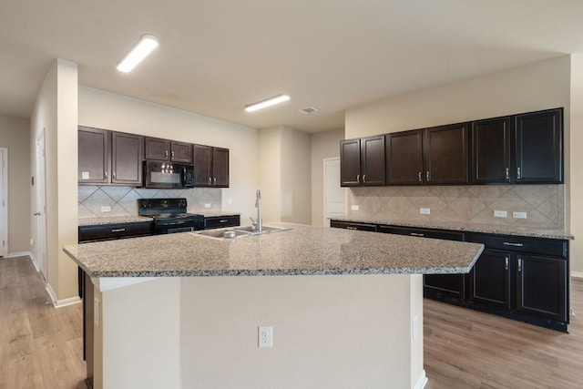 15212 Shell Bark Cv, Austin, TX 78724 - kitchen with black appliances, light wood-style floors, decorative backsplash, and an island with sink