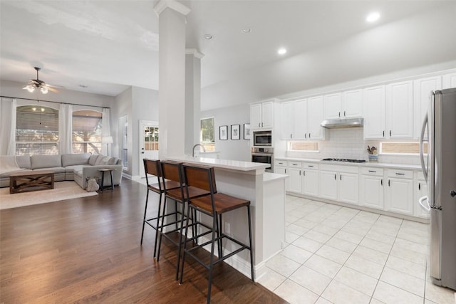 10408 Hansa Dr, Austin, TX 78739 - kitchen with stainless steel appliances, under cabinet range hood, open floor plan, a kitchen breakfast bar, and white cabinets