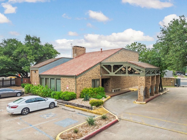 8888 Tallwood Dr Unit 1202, Austin, TX 78759 - view of front facade with a tile roof, uncovered parking, brick siding, and a chimney
