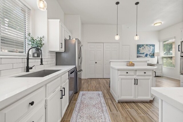 2901 Rochelle Dr, Austin, TX 78748 - kitchen featuring appliances with stainless steel finishes, light wood-style flooring, tasteful backsplash, white cabinets, and a center island