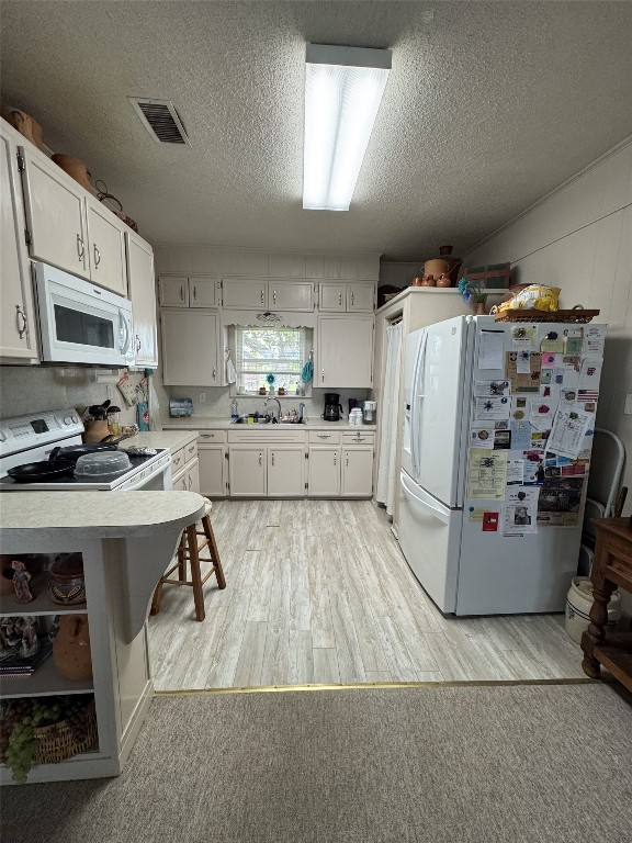 549 Marshall Johnson Ave S, Port Lavaca, TX 77979 - kitchen with white appliances, light wood-type flooring, light countertops, a textured ceiling, and white cabinets