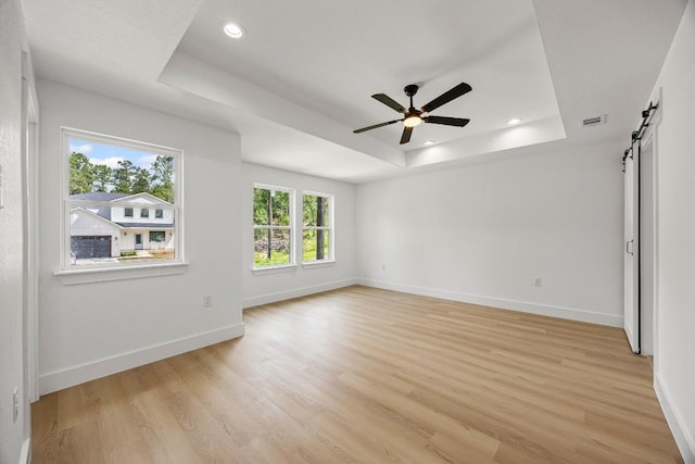 161 Honopu Dr, Bastrop, TX 78602 - empty room featuring a tray ceiling, a barn door, light wood-style floors, ceiling fan, and recessed lighting
