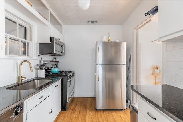 1028 E 43rd St, Austin, TX 78751 - kitchen with appliances with stainless steel finishes, white cabinetry, light wood finished floors, dark stone counters, and tasteful backsplash