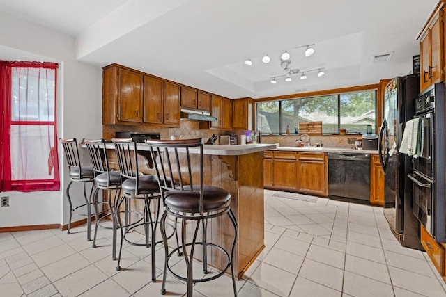1303 Creekview Dr, Round Rock, TX 78681 - kitchen with black appliances, a peninsula, under cabinet range hood, brown cabinetry, and light tile patterned floors