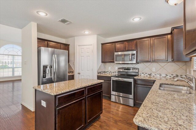 3211 Malmaison Rd, Killeen, TX 76542 - kitchen featuring appliances with stainless steel finishes, dark brown cabinets, light stone countertops, a center island, and backsplash