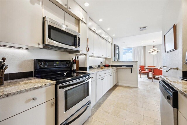 1801 Lavaca St Unit 9J, Austin, TX 78701 - kitchen with appliances with stainless steel finishes, a chandelier, a peninsula, light tile patterned floors, and white cabinets