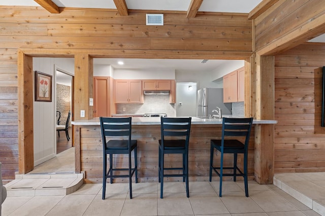 2609 Ellise Ave, Austin, TX 78757 - kitchen with wood walls, freestanding refrigerator, under cabinet range hood, a breakfast bar area, and a peninsula