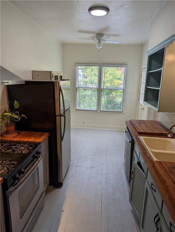 308 Taylor Rd, Elgin, TX 78621 - kitchen featuring wooden counters, stainless steel appliances, wall chimney range hood, ceiling fan, and light wood-style flooring
