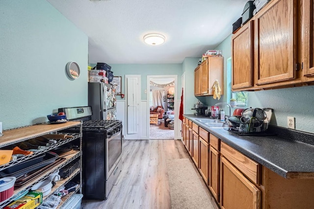 5605 Tura Ln, Austin, TX 78721 - kitchen with stainless steel appliances, light wood-type flooring, brown cabinets, dark countertops, and a textured wall