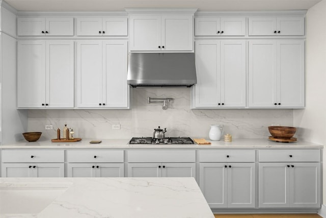 8405 Ambergill Ct, Austin, TX 78744 - kitchen featuring under cabinet range hood, stainless steel gas cooktop, white cabinets, light stone counters, and backsplash