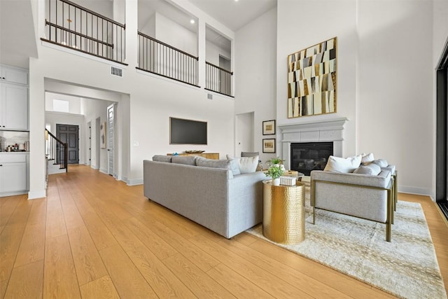 8405 Ambergill Ct, Austin, TX 78744 - living room featuring a high ceiling, a glass covered fireplace, light wood-type flooring, and stairs