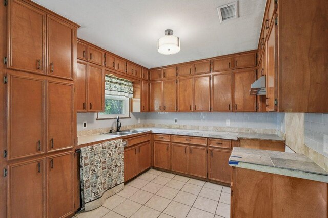 709 Harvey Ave, Burnet, TX 78611 - kitchen with brown cabinetry, under cabinet range hood, and decorative backsplash