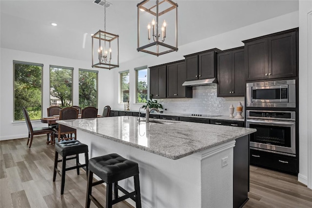 1404 Scenic Oaks Dr, Georgetown, TX 78628 - kitchen with appliances with stainless steel finishes, tasteful backsplash, light stone counters, an island with sink, and a kitchen breakfast bar
