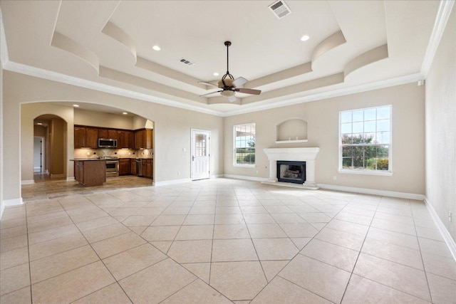144 Escondido Dr, Del Valle, TX 78617 - unfurnished living room with ceiling fan, a tray ceiling, light tile patterned floors, arched walkways, and a fireplace with raised hearth