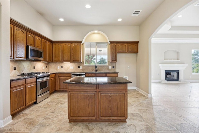 144 Escondido Dr, Del Valle, TX 78617 - kitchen featuring appliances with stainless steel finishes, dark stone counters, a center island, brown cabinets, and arched walkways