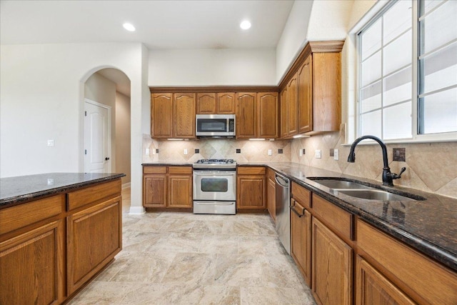 144 Escondido Dr, Del Valle, TX 78617 - kitchen with stainless steel appliances, dark stone countertops, brown cabinetry, arched walkways, and tasteful backsplash