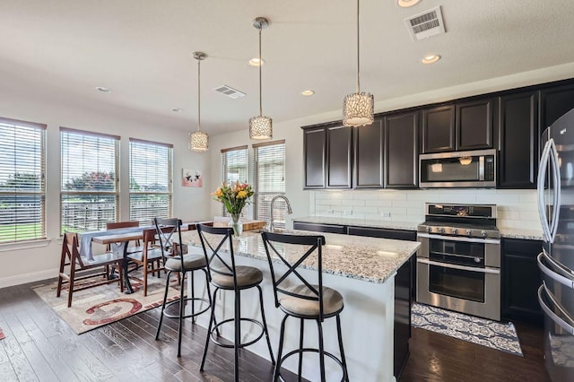 3025 Lions Tail St, Austin, TX 78728 - kitchen featuring appliances with stainless steel finishes, a kitchen island with sink, decorative backsplash, light stone countertops, and recessed lighting