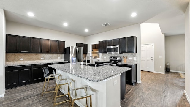 201 Garcitas Creek Ln, Hutto, TX 78634 - kitchen with appliances with stainless steel finishes, a kitchen island with sink, tasteful backsplash, dark wood-type flooring, and light stone countertops