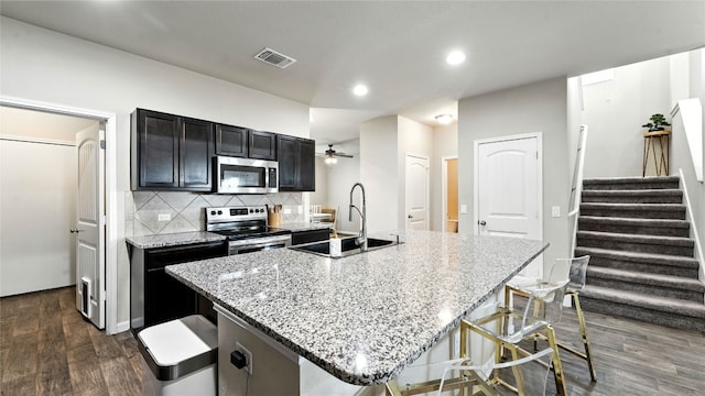 201 Garcitas Creek Ln, Hutto, TX 78634 - kitchen with stainless steel appliances, dark wood-style flooring, a kitchen island with sink, decorative backsplash, and light stone countertops