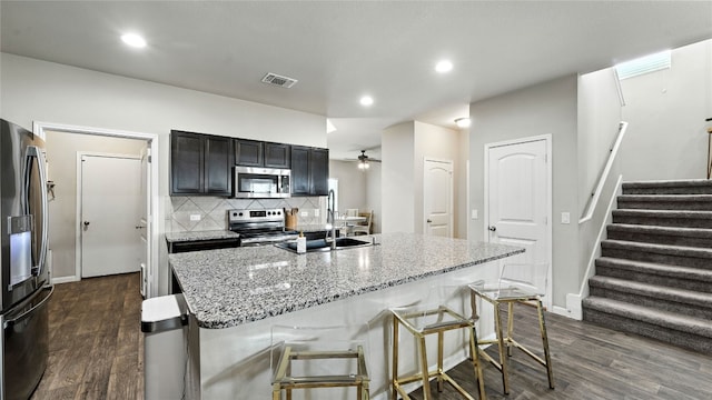 201 Garcitas Creek Ln, Hutto, TX 78634 - kitchen featuring appliances with stainless steel finishes, dark wood-type flooring, a kitchen bar, backsplash, and light stone countertops