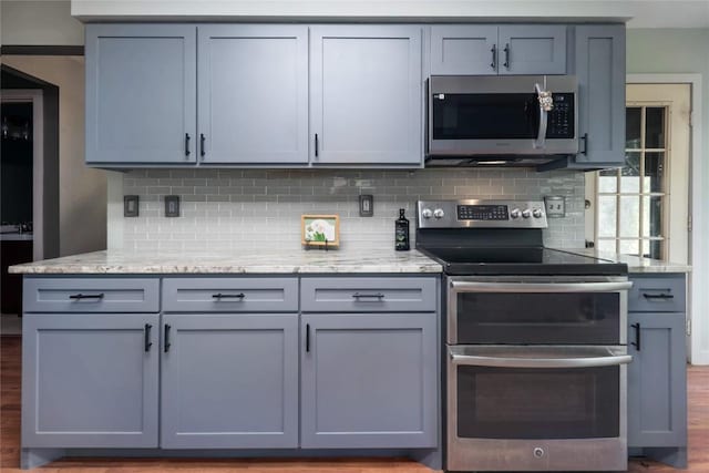 1912 Gaylord Dr, Austin, TX 78728 - kitchen with appliances with stainless steel finishes, tasteful backsplash, gray cabinetry, light stone countertops, and wood finished floors