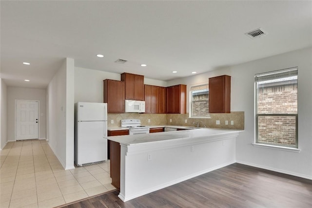 933 Oatmeal Dr, Pflugerville, TX 78660 - kitchen with white appliances, light countertops, tasteful backsplash, a peninsula, and light wood finished floors