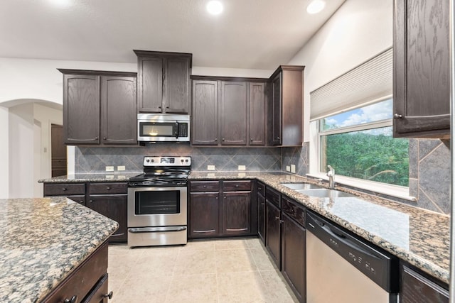 851 Stone Mountain Dr, Marble Falls, TX 78654 - kitchen with stainless steel appliances, dark stone countertops, dark brown cabinetry, tasteful backsplash, and arched walkways
