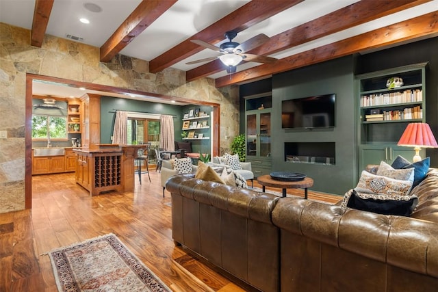 79 Saddle Rock Rdg, Wimberley, TX 78676 - living room featuring beam ceiling, light wood-type flooring, a ceiling fan, a fireplace, and built in shelves