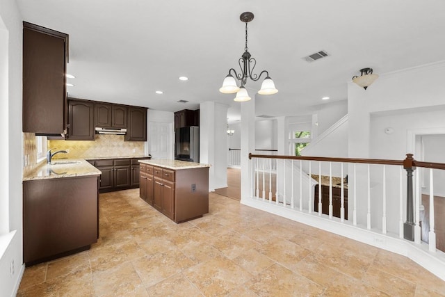 10504 Grand Oak Cir, Austin, TX 78750 - kitchen featuring under cabinet range hood, fridge, a chandelier, decorative backsplash, and dark brown cabinetry