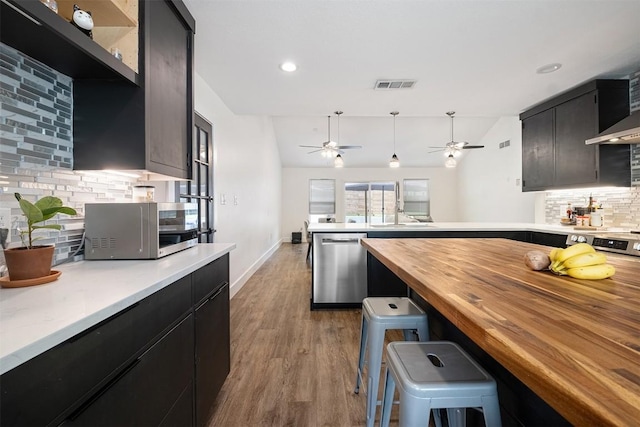 13516 Caldwell Dr, Austin, TX 78750 - kitchen featuring stainless steel appliances, wood counters, decorative backsplash, a peninsula, and dark cabinetry