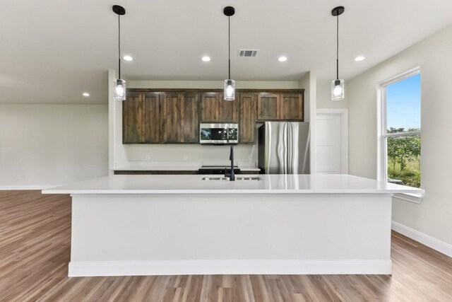 130 Mokalau Dr, Bastrop, TX 78602 - kitchen with appliances with stainless steel finishes, light countertops, a center island with sink, light wood finished floors, and recessed lighting