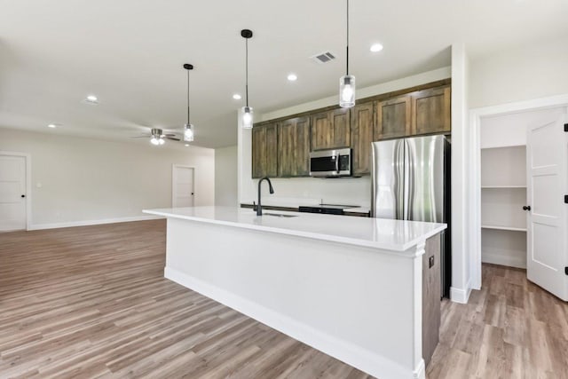 130 Mokalau Dr, Bastrop, TX 78602 - kitchen featuring appliances with stainless steel finishes, light wood finished floors, a ceiling fan, light countertops, and an island with sink