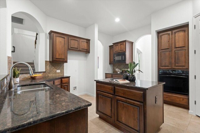 211 Longmont Ln, Austin, TX 78737 - kitchen featuring black appliances, arched walkways, decorative backsplash, a kitchen island, and dark stone counters
